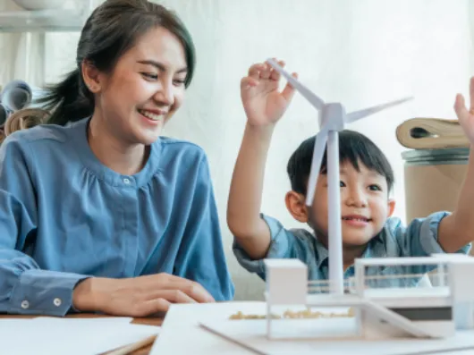 A boy in a classroom playing with a model wind turbine